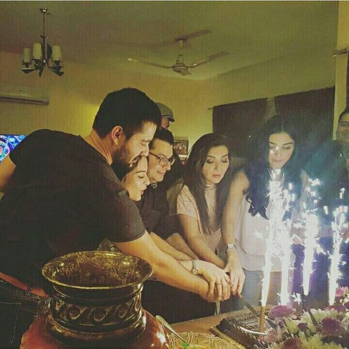 a group of people standing around a cake with lit candles