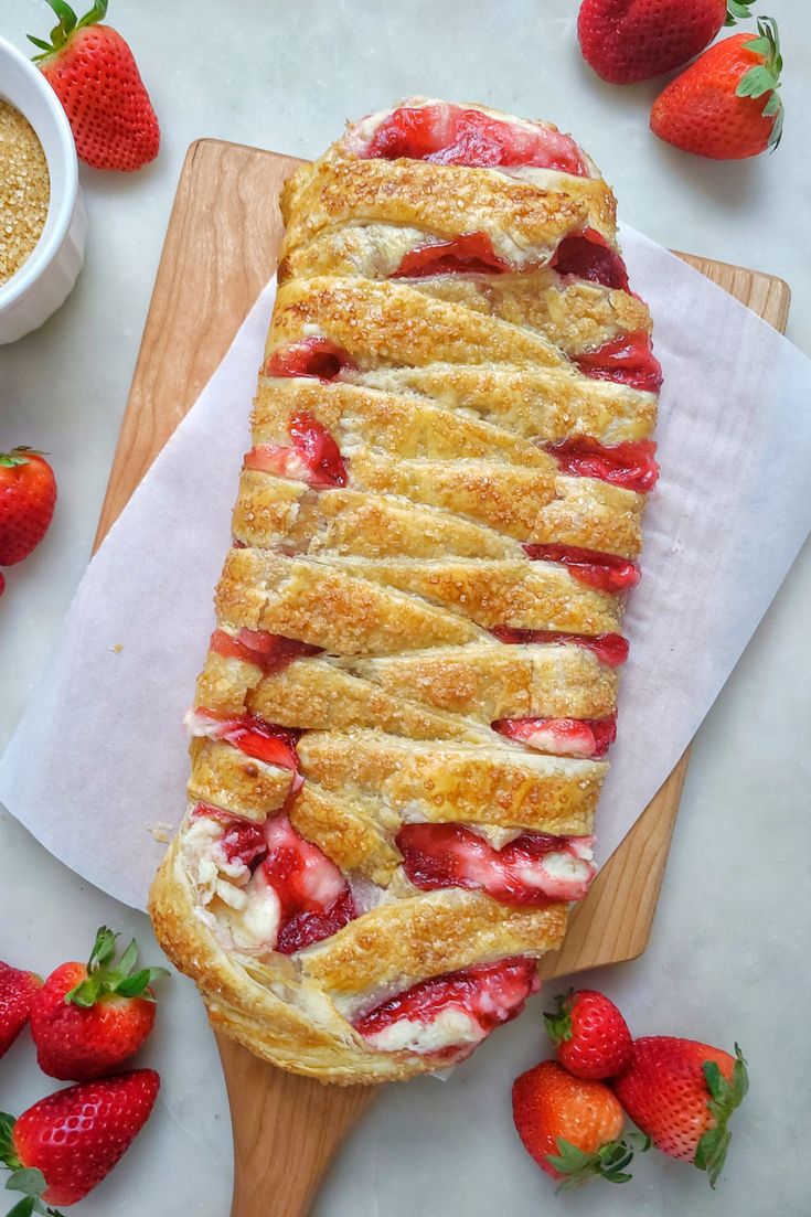 a pastry with strawberries on it sitting on top of a cutting board next to some other food