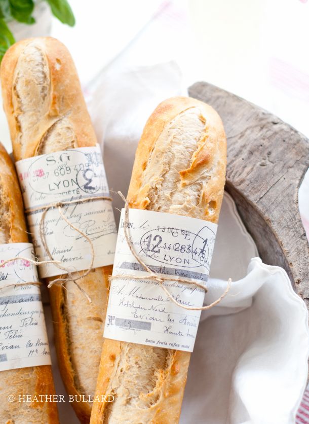 three sub sandwiches wrapped in twine and tied with paper on top of a white plate