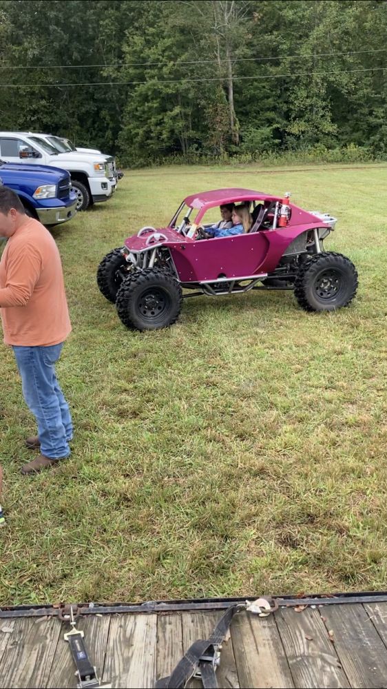 two men standing next to a pink buggy on top of a grass covered field