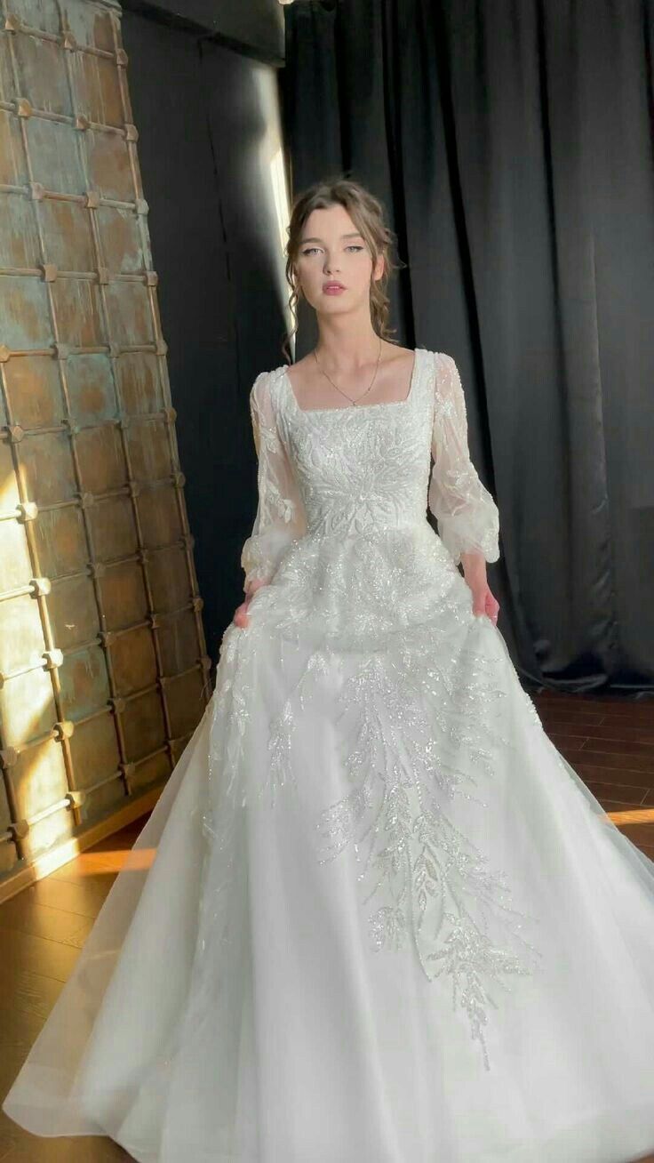 a woman in a white wedding dress standing on a wooden floor with her hands behind her back