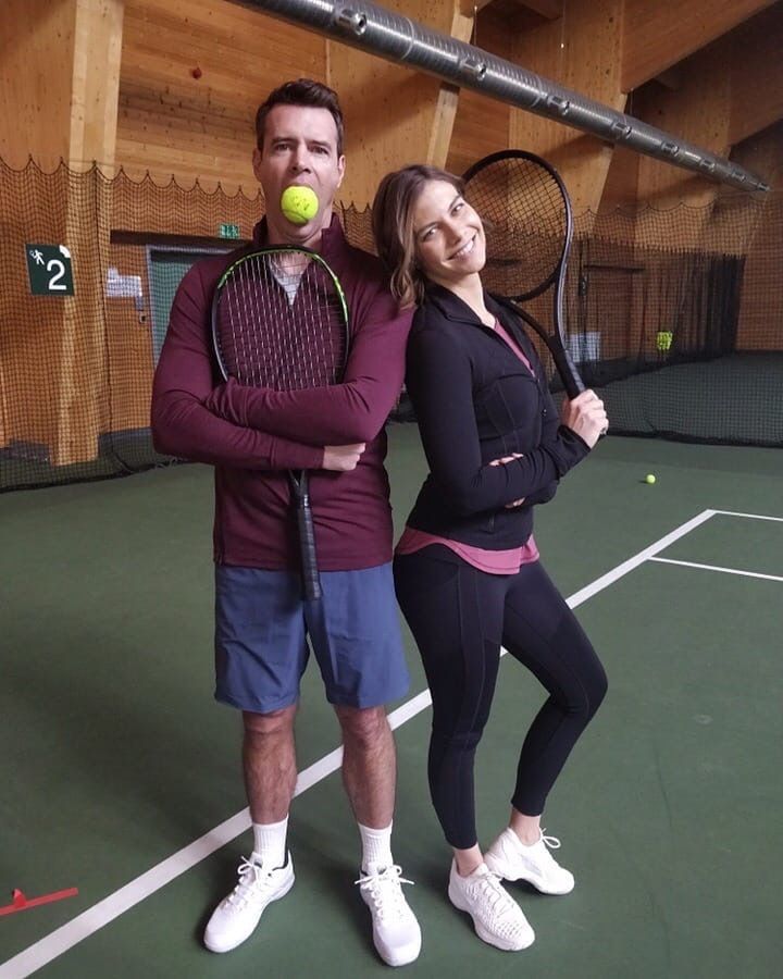 a man and woman standing on a tennis court with rackets in their hands, posing for the camera