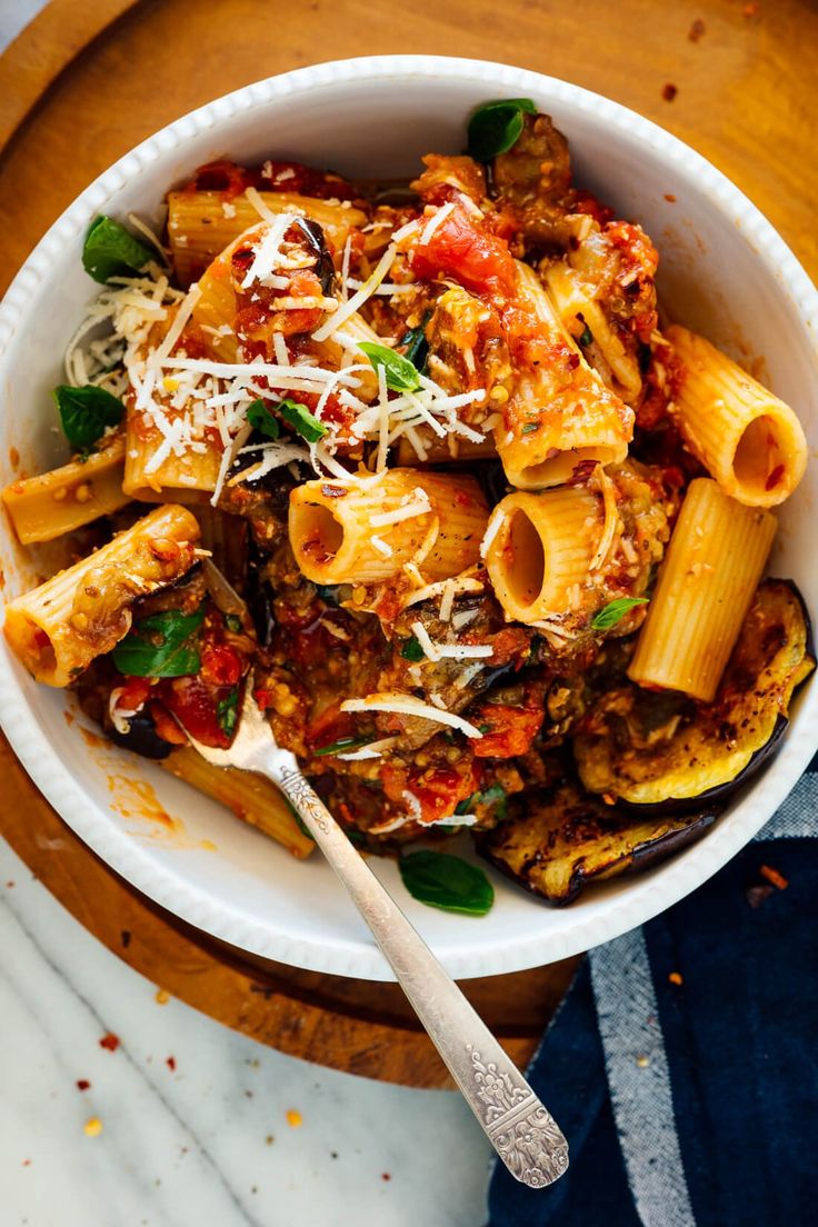 a white bowl filled with pasta and sauce on top of a wooden cutting board next to a blue towel