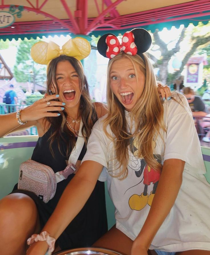 two women pose for the camera with mickey mouse ears on their heads at an amusement park