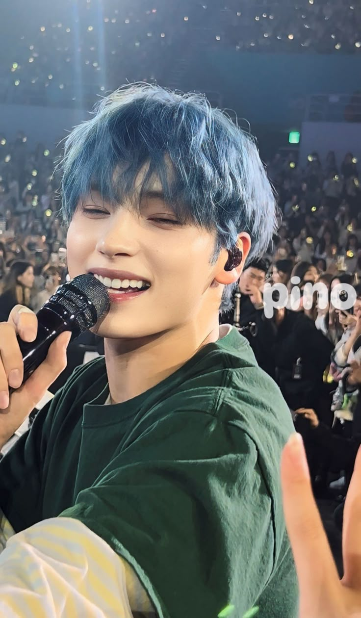 a man with blue hair holding a microphone in front of an audience at a concert