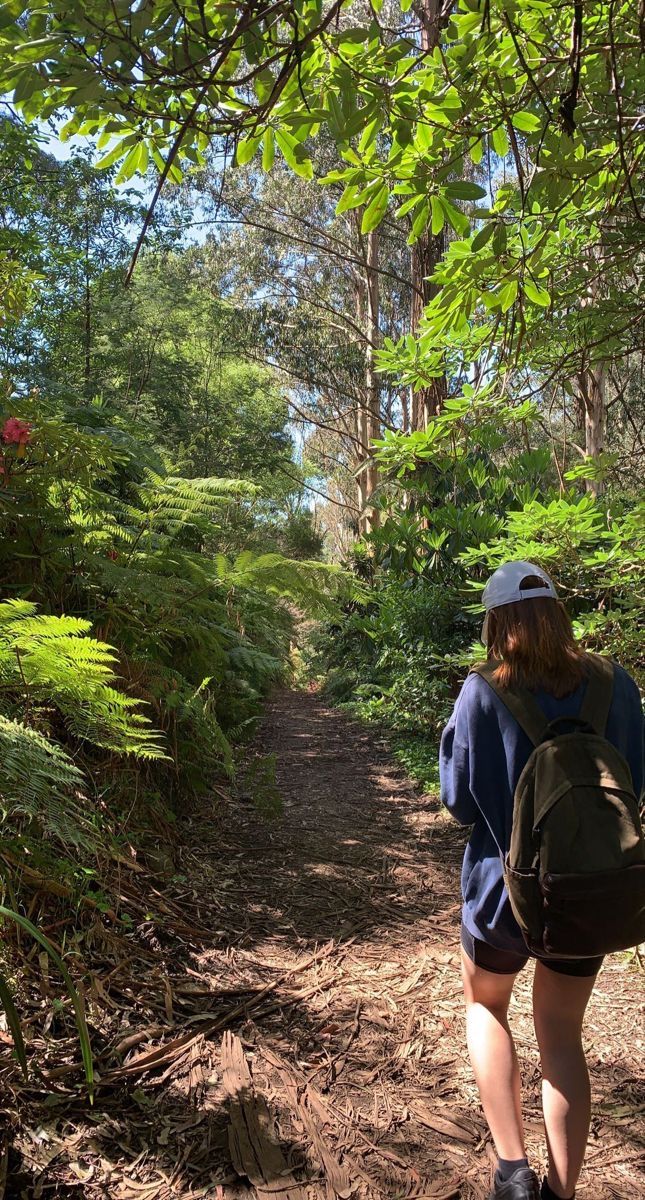 a woman with a backpack walking down a trail in the woods