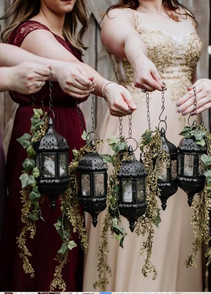 three women in dresses are holding lanterns with plants hanging from them