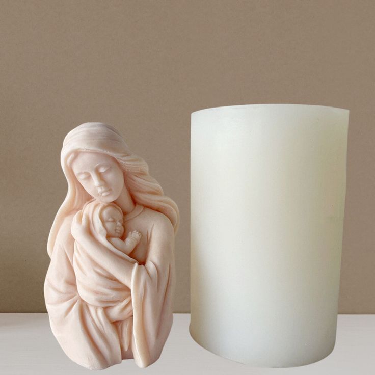 a white candle next to a statue of a woman holding a baby