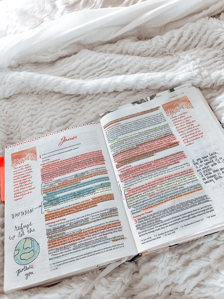 an open bible laying on top of a bed next to a red marker and pen