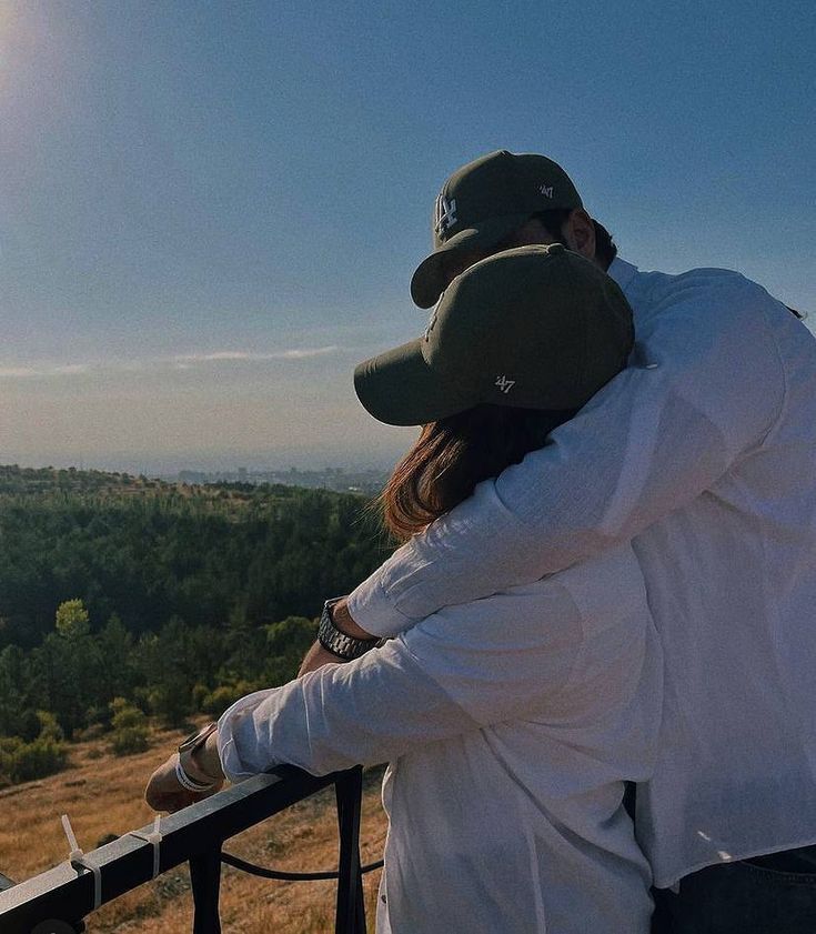 two people standing on top of a hill looking out at the trees and hills in the distance