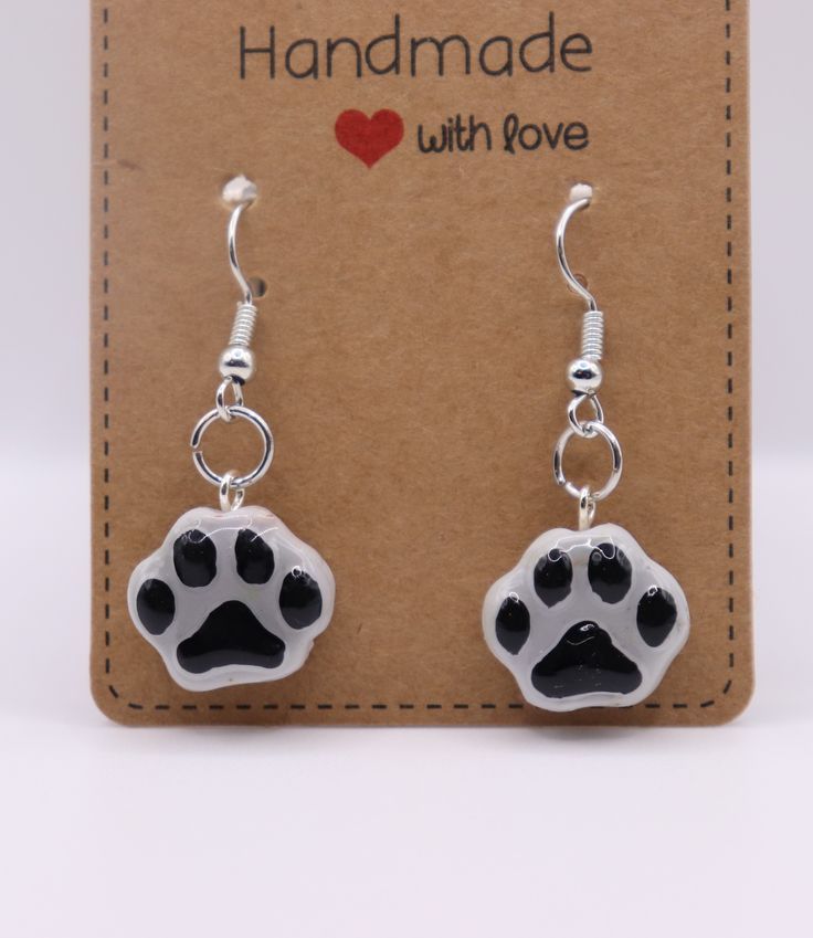 a pair of black and white paw prints dangling from silver earwires on a card