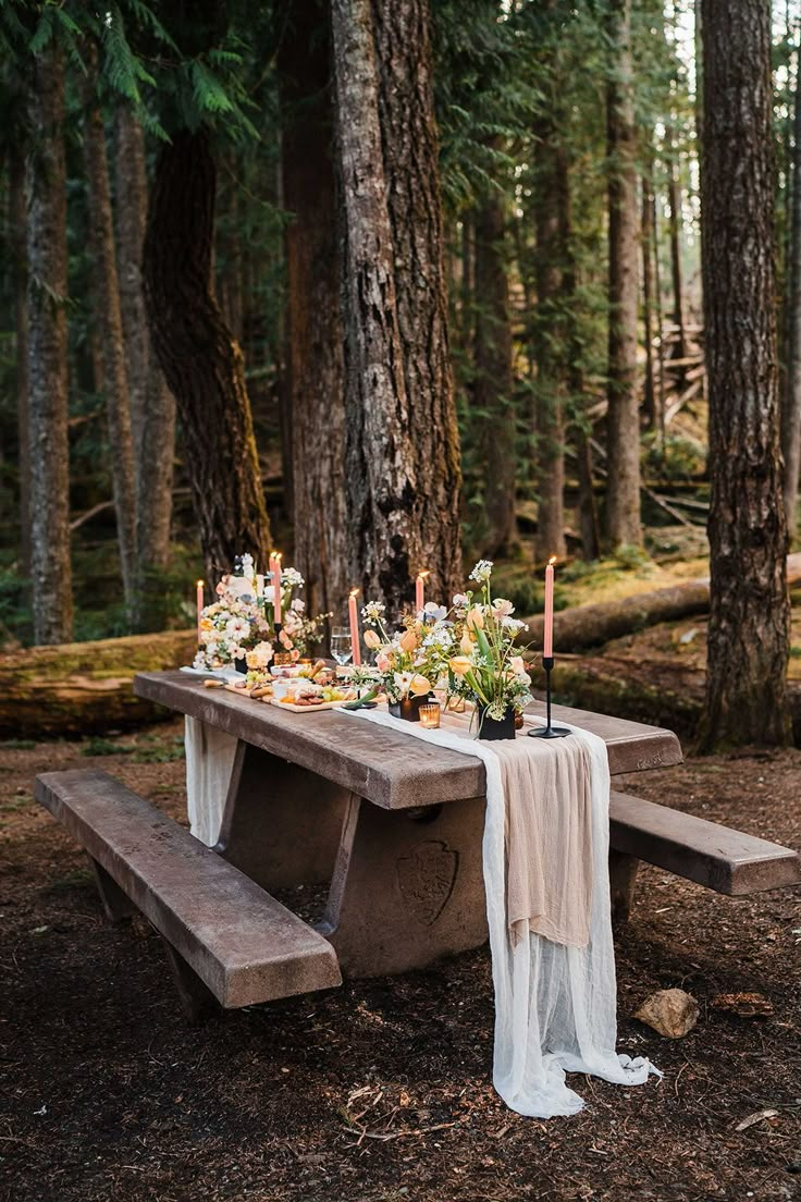 a table with flowers and candles is set up in the woods for an outdoor dinner