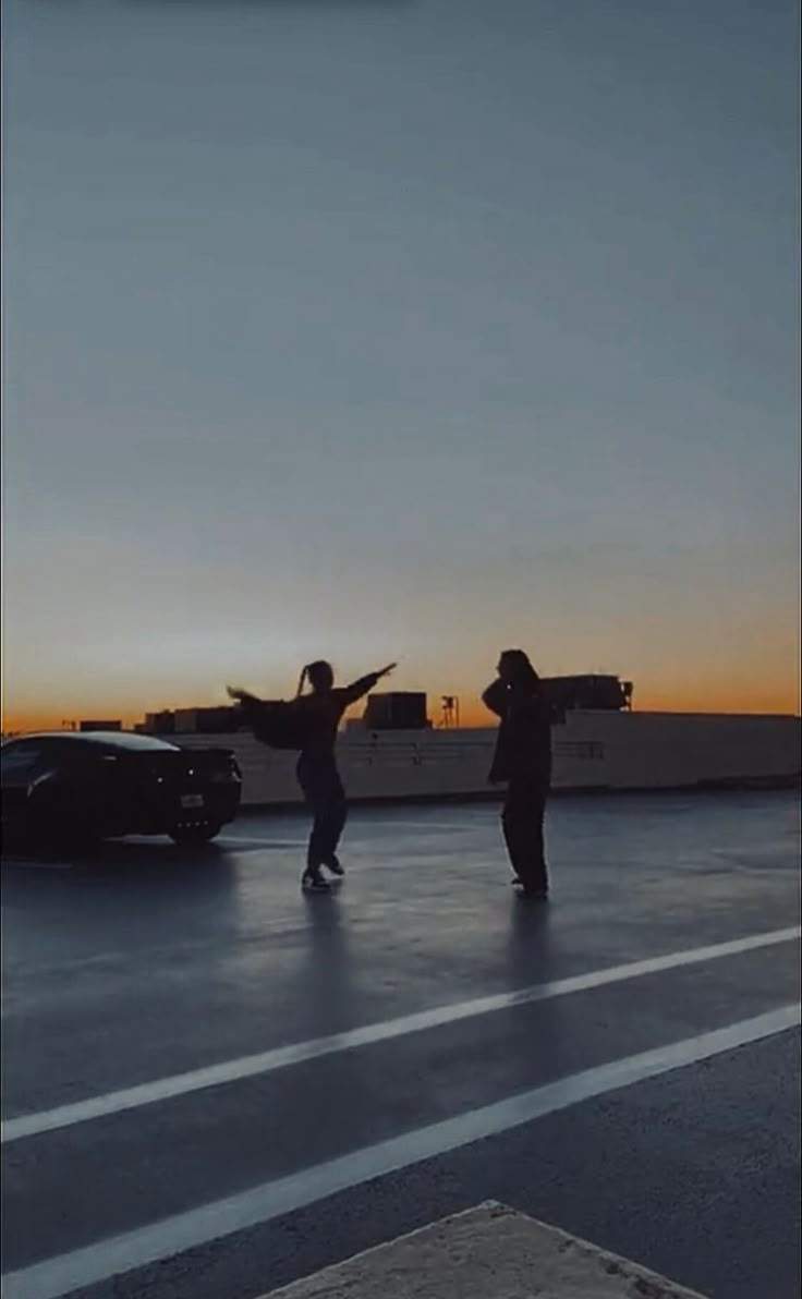 two people standing in the middle of an empty parking lot with their arms out to each other