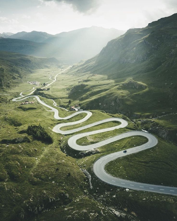 an aerial view of a winding road in the mountains with sun shining down on it