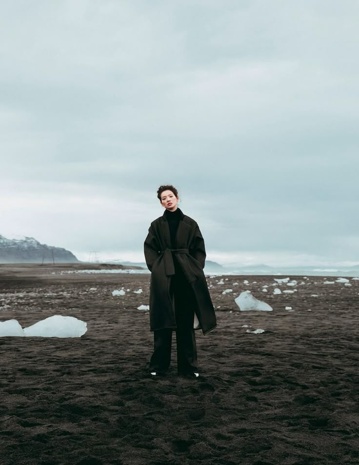 a man standing on top of a sandy beach next to icebergs in the distance