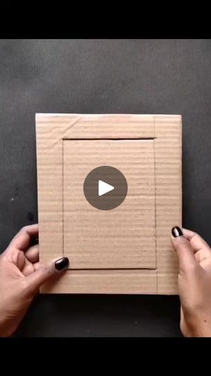 two hands holding up a cardboard box with an image of a video playing on it