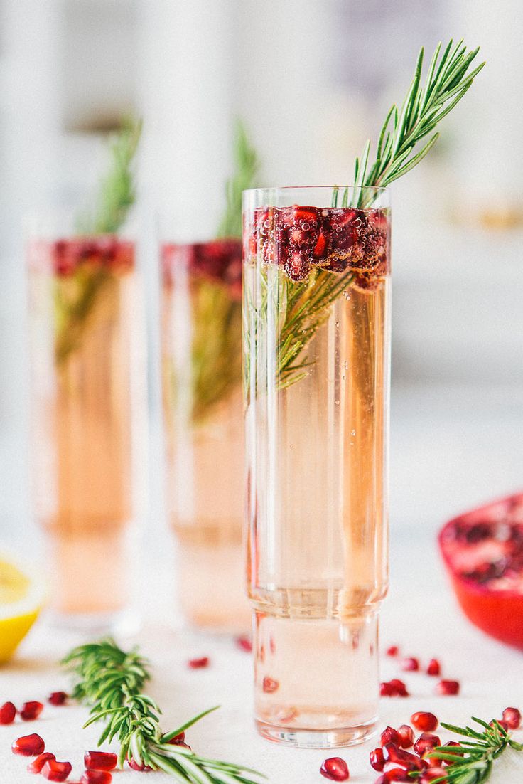 two glasses filled with wine and garnished with rosemary, lemons and pomegranate