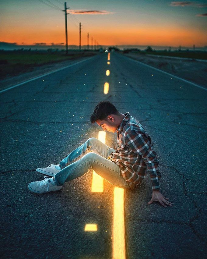 a young man sitting on the side of an empty road