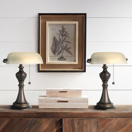 two lamps sitting on top of a wooden dresser next to a framed picture and books