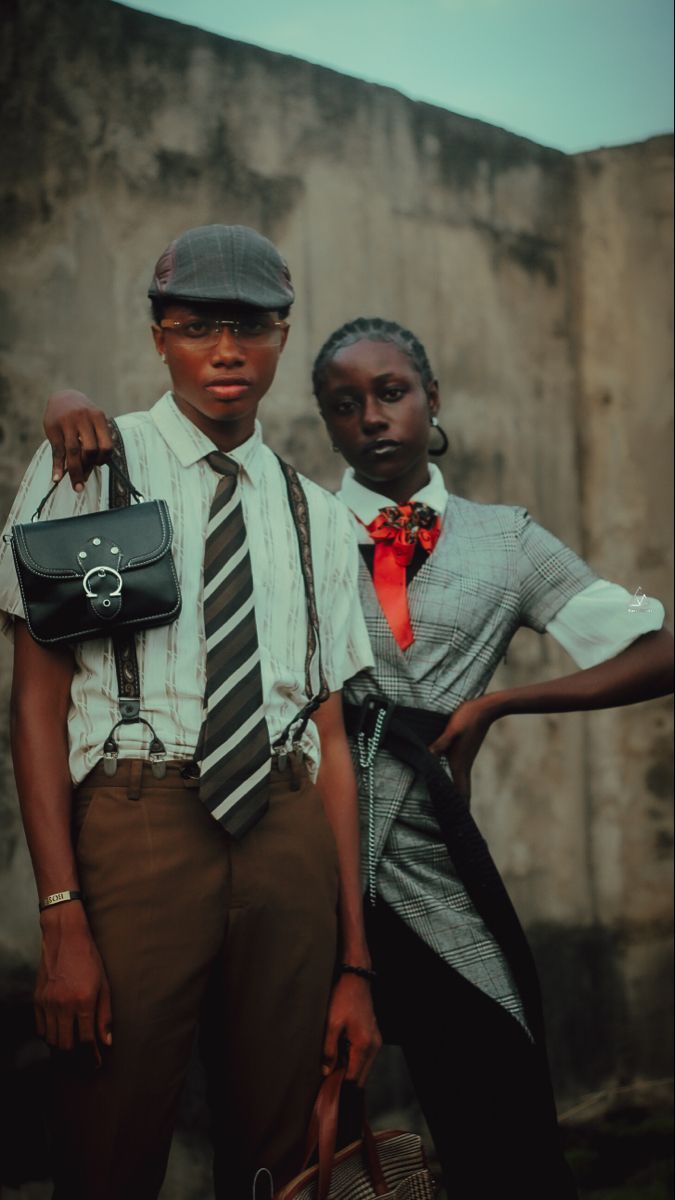 two people standing next to each other with one holding a purse and the other wearing a hat