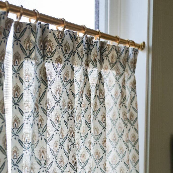 the curtain is hanging in front of the window with an ornate pattern and gold hardware