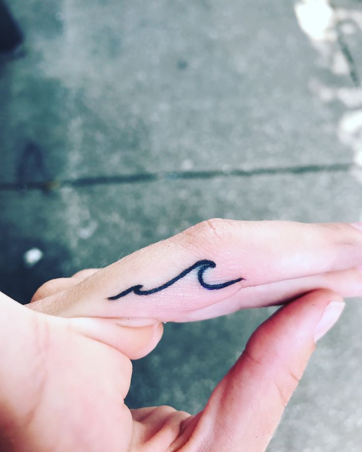 a person with a small wave tattoo on their finger