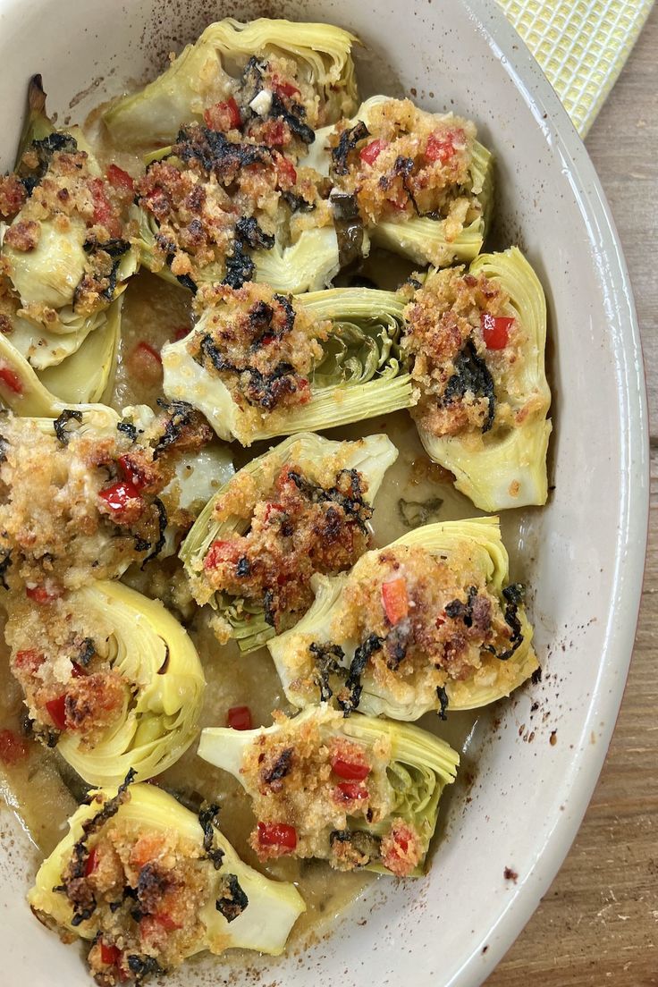 a white bowl filled with artichokes covered in sauce and seasoning sitting on top of a wooden table