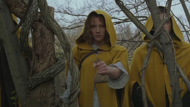 two people in yellow coats standing next to each other near some trees and branches with no leaves on them