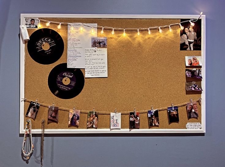 a bulletin board with pictures and records hanging on it's sides, surrounded by string lights