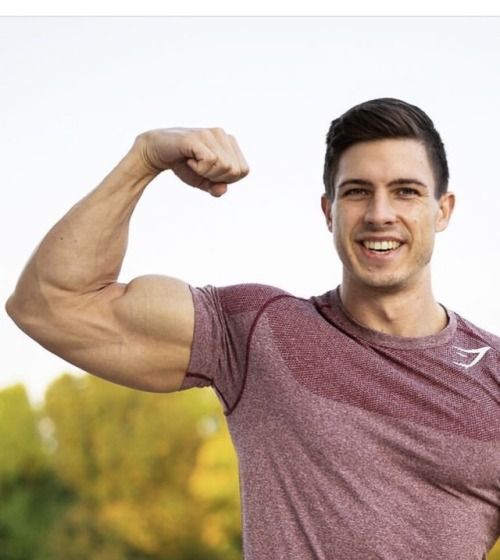 a young man flexing his muscles in front of the camera with trees in the background