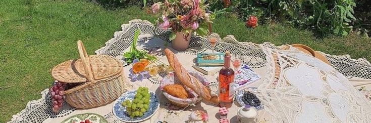 a picnic table with food and drinks on it in the grass next to some bushes