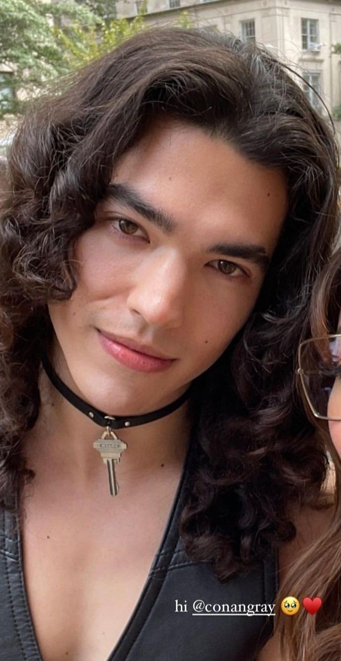 two people are posing for the camera with one wearing a necklace and the other wears glasses