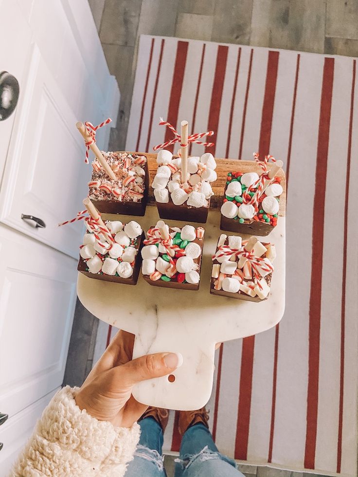 a person holding up a cake with marshmallows and candy canes on it