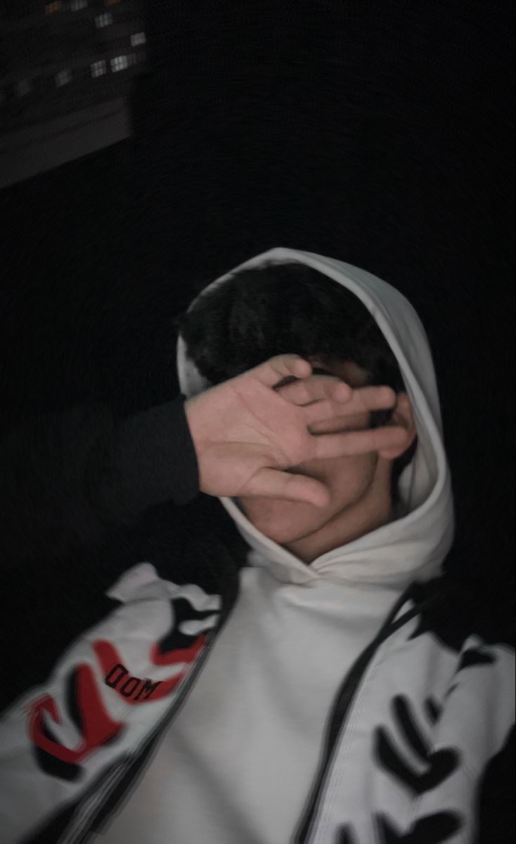 a person in a hoodie covering their face with both hands and holding the other hand