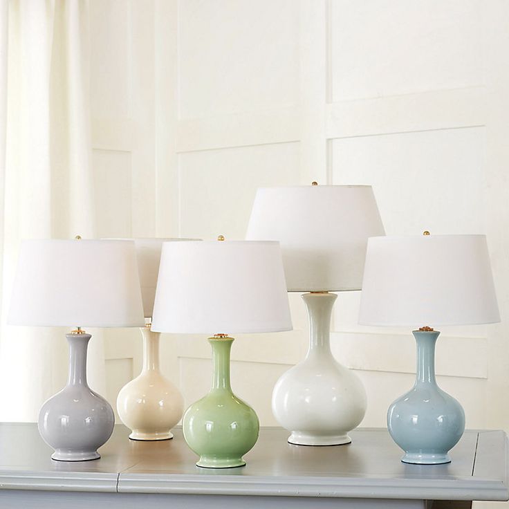 five different colored vases sitting on top of a table next to a window with white curtains