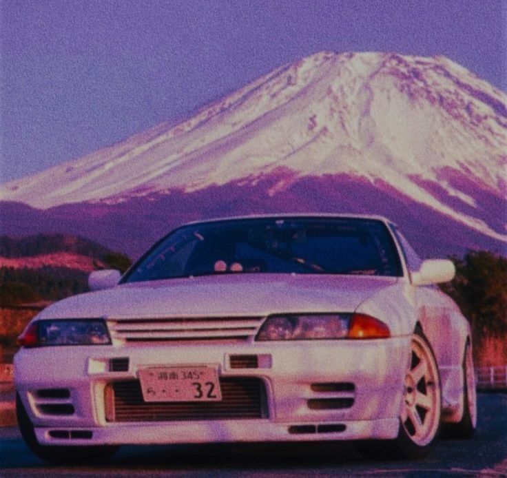 a white car is parked in front of a mountain with snow on it's top