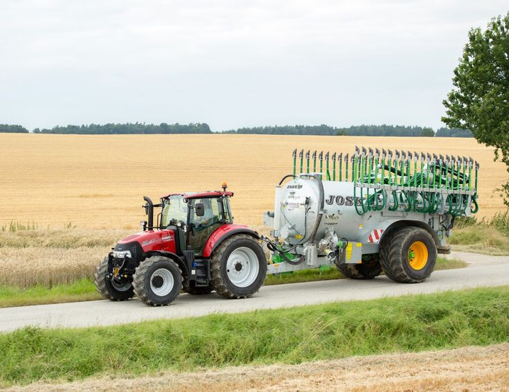 a tractor pulling a sprayer behind it down a road in front of a wheat field