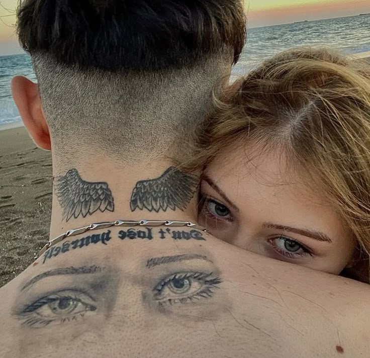 a man and woman with tattoos on their neck looking into the distance at the ocean