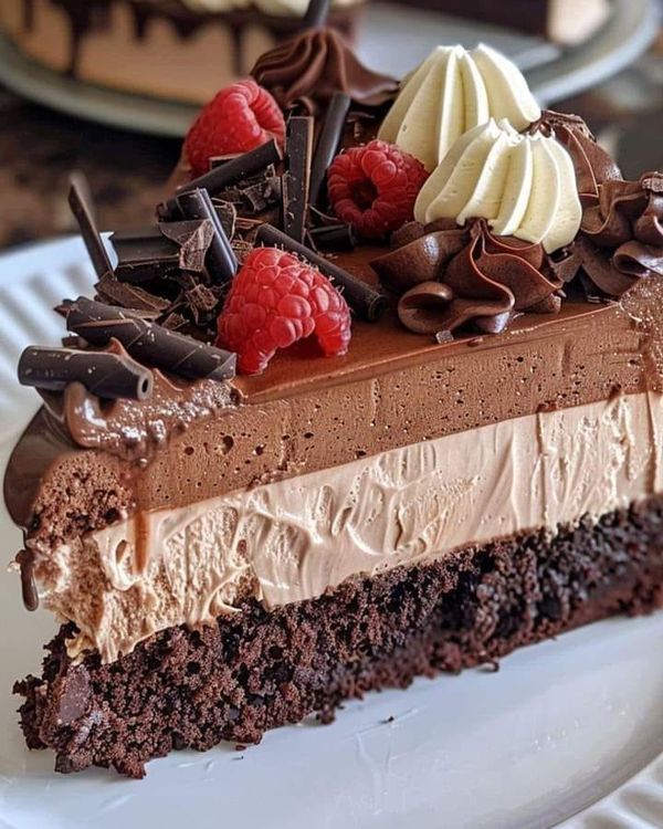 a piece of chocolate cake with whipped cream and raspberries on top is sitting on a white plate