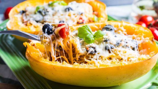 spaghetti dish stuffed in an eggplant on a green platter with fork and serving utensils