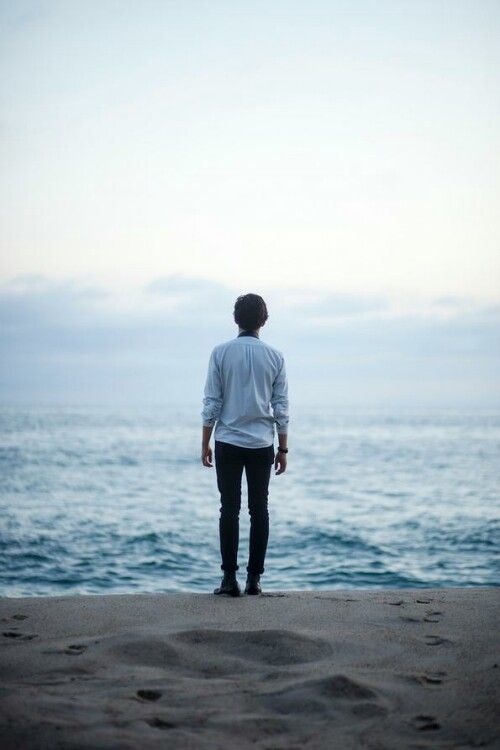 a man standing on top of a sandy beach next to the ocean with his back to the camera