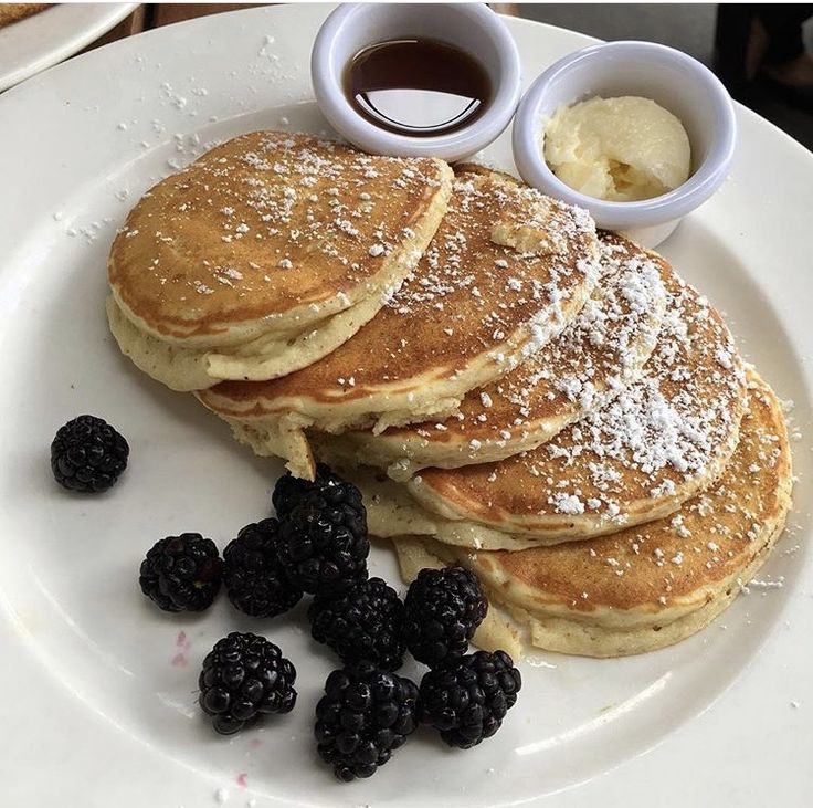 pancakes and blackberries on a plate with syrup, butter and powdered sugar for toppings