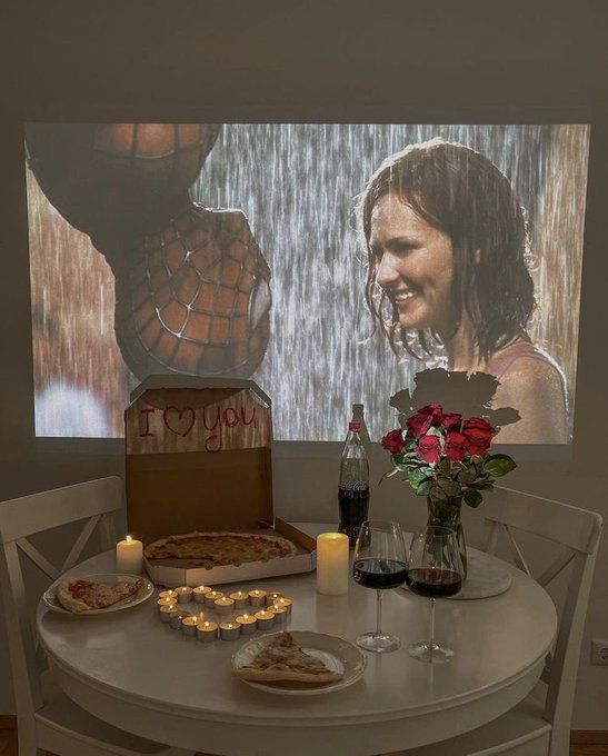 a table topped with pizza and candles next to a wall mounted screen that reads i love you