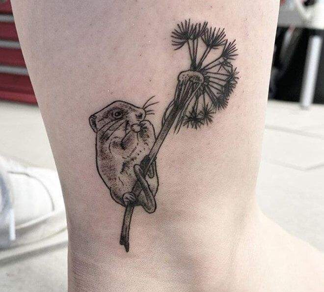 a small black and white tattoo of a cat holding a dandelion