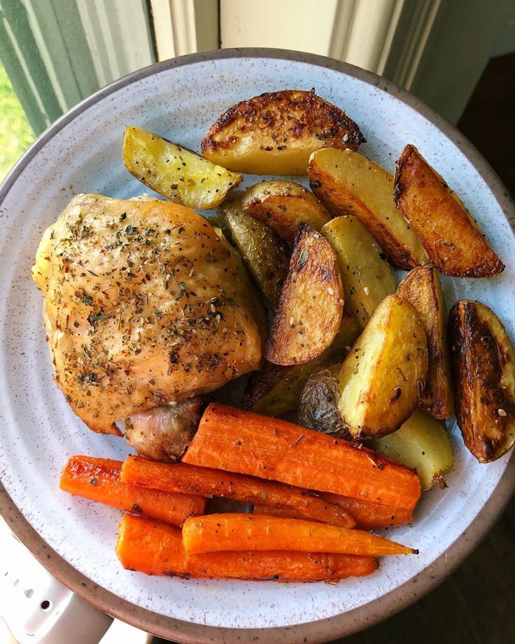 a plate with chicken, potatoes and carrots on it next to a window sill