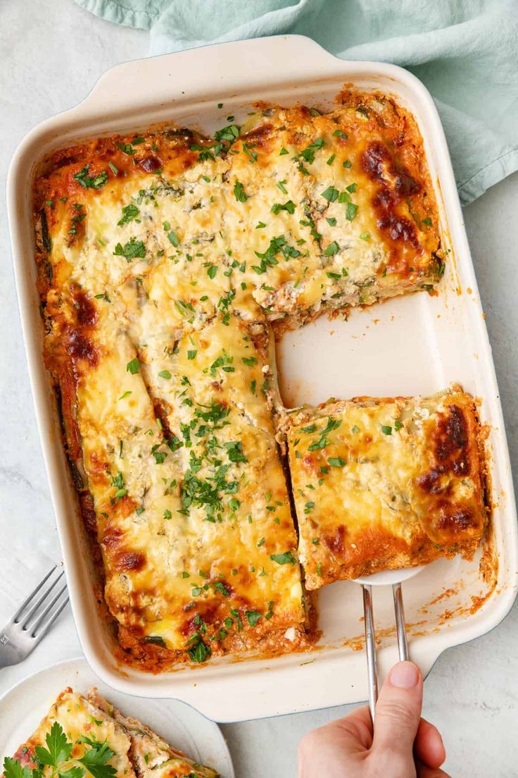 a person holding a fork over a casserole dish with cheese and parsley