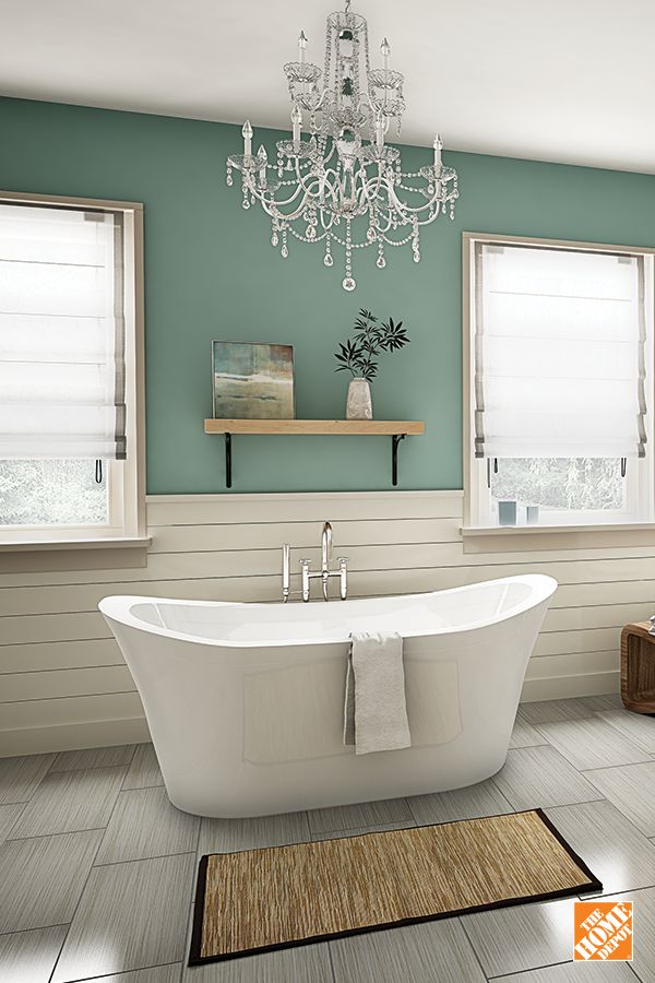 a white bath tub sitting under a chandelier in a bathroom next to two windows