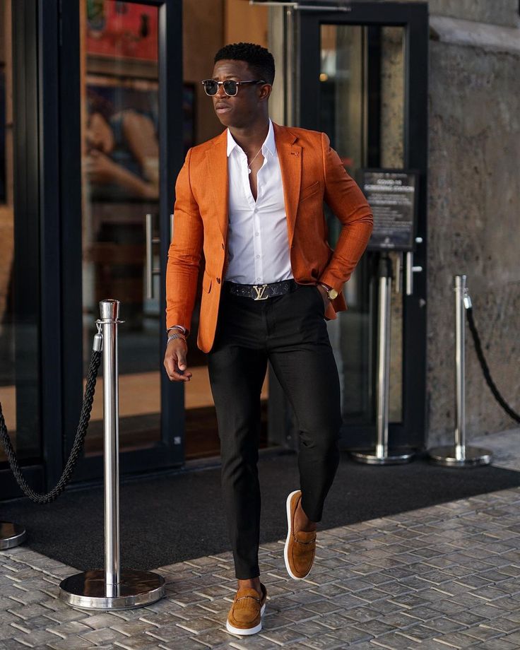 a man in an orange blazer and white shirt is walking down the street with his hands on his hips