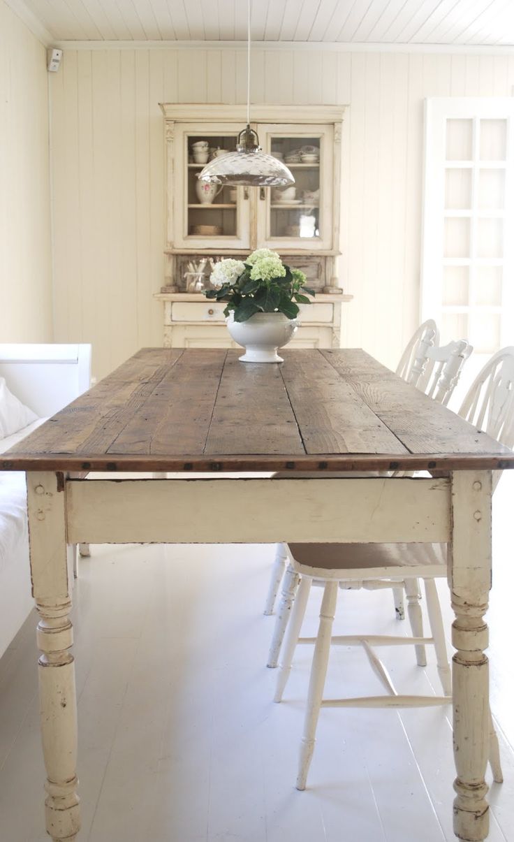 a wooden table sitting in the middle of a room with white chairs and a potted plant on top of it