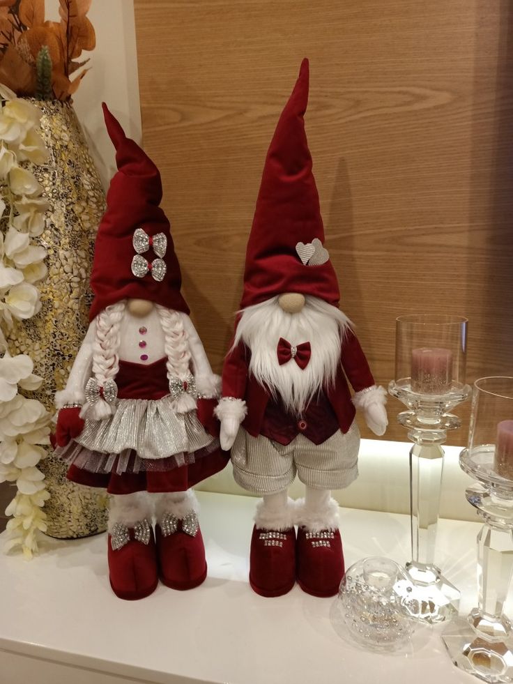 two red and white gnomes sitting next to each other on a table with wine glasses